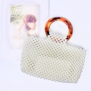 Detail of handmade pearl beaded handbag with amber resin ring handle on white background