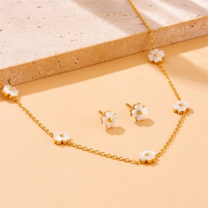 Elegant gold jewelry set with white flower pendant necklace and stud earrings on stone