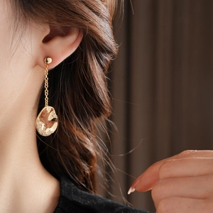 Détail d'une boucle d'oreille asymétrique dorée avec chaîne et pendentif givré sur modèle