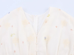 Détail du col en V avec broderie florale et boutons en perles décoratives sur mousseline