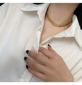 Détail d'un collier plat doré avec pendentif GOOD LUCK porté par un mannequin