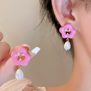 Détail de boucles d'oreilles fleur rose avec strass et pendentif perle blanche