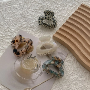 Flat lay of four tortoiseshell and marble acetate hair claws on textured paper