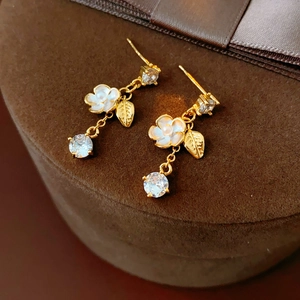 Detailed close-up of gold-plated flower tassel earrings on brown velvet jewelry box