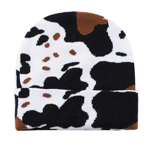 Detailed close-up of cow print knit beanie showing black and brown spots on white fabric