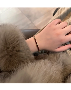 Dettaglio macro di un bracciale in pelle intrecciata rossa con nodi dorati sul polso femminile