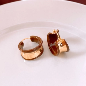 Detail view of 18k gold plated round drop oil earrings with brown resin on white ceramic