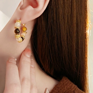 Close-up of vintage gold hoop earrings with white and tiger eye stones on a model