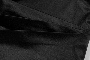 Macro detail of glossy black pleated satin fabric showing smooth texture and layered folds