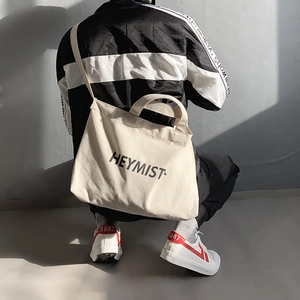 Detailed back view of a person wearing a beige canvas crossbody bag with HEYMIST logo