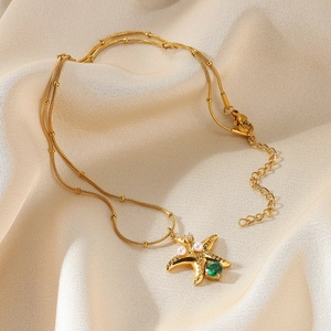 Detail of gold layered necklace featuring a starfish pendant with green gem and white pearl