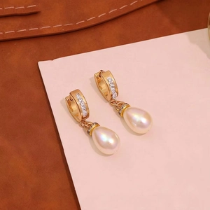 Close-up of golden pearl drop earrings with sparkling cubic zirconia on a warm background