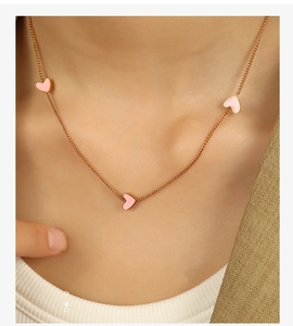 Close-up of three pink enamel hearts on a golden necklace worn by a female model