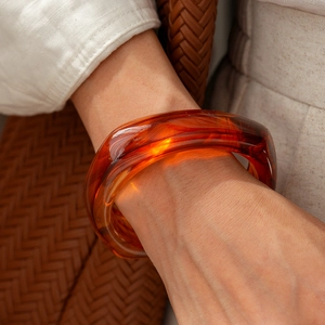 Detail of amber acrylic bangle on wrist with neutral textured fabric background