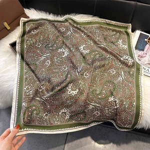 Vue macro d'un foulard carré en soie à motif paisley avec détails vert et caramel