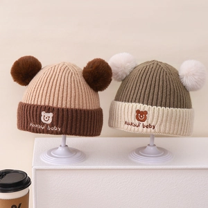 Detail von gestrickten Babymützen mit Kunstfellbommeln und süßer Bärenstickerei für den Winter