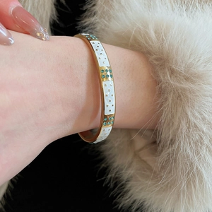 Détail macro du bracelet doré avec émail blanc, motifs d'étoiles et zircons bleus