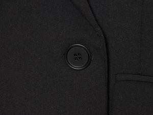 Gros plan d'un blazer noir montrant la texture du sergé et un bouton rond classique