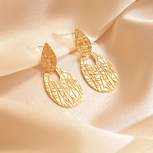 Close-up of golden teardrop earrings with a textured crackle finish on beige silk fabric