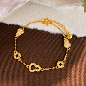 Bracelet plaqué or avec breloques gourde en zircone et pièces de monnaie sur fond texturé