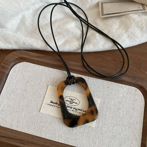 Detail of tortoise shell resin pendant with a minimalist black cord on a wooden tray