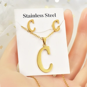 Dettaglio ravvicinato di collana e orecchini a lettera C in acciaio dorato sulla mano