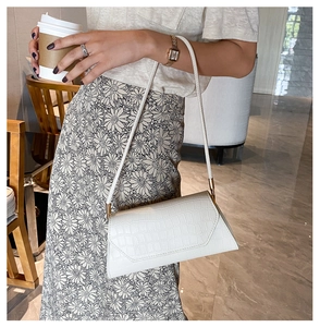 Detail of white crocodile pattern baguette bag worn over the shoulder with gold hardware