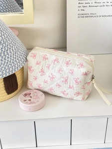 Close-up of quilted cotton cosmetic bag featuring pink bow patterns and a zipper puller