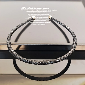 Macro detail of slim black crystal headband with gold metal ends on a reflective surface