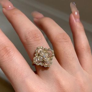 Close-up of golden clover ring featuring central pearl and sparkling zircon accents