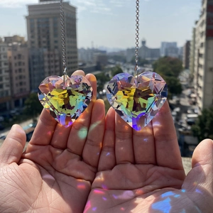 Close-up of hand holding two heart-shaped K9 crystal suncatchers with rainbow reflections