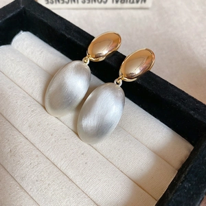Detailed macro shot of two-tone oval earrings with gold studs and silver brushed texture