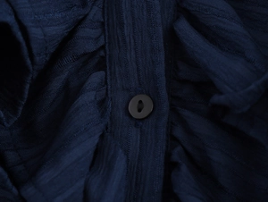Close-up of deep blue textured fabric featuring a black button on the front placket