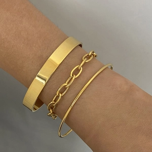 Set aus goldenen Edelstahlarmbändern und Gliederkette am Handgelenk im minimalistischen Stil