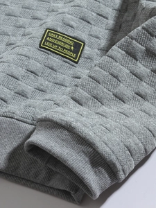 Detail of grey quilted checkered sweatshirt showing ribbed cuffs and textile brand label
