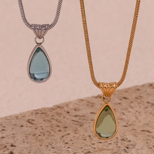 Detailed view of teardrop crystal pendants in gold and silver snake chains on stone base