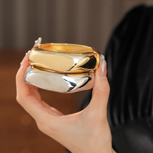 Detailed view of polished wide chunky bracelets in gold and silver metallic finishes