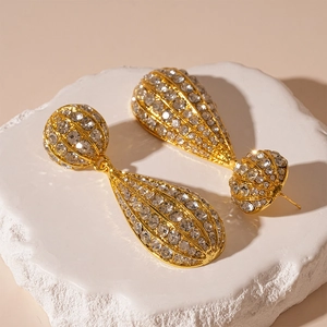 Close-up of golden teardrop earrings with pave crystals on a white textured stand