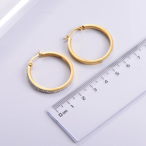 Close-up of gold hoop earrings with zircon stones and a ruler for 3cm size reference