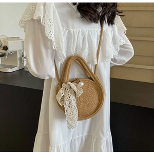 Detail of round straw bag with white lace scarf bow and elegant pearl charm