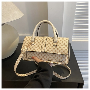Detail of cream crossbody bag with brown pattern and adjustable strap on a dark desk