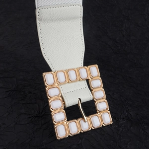 Detail of white elastic waist belt with a gold buckle and white acrylic gemstone
