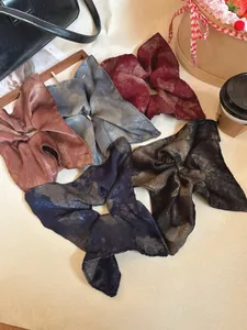 Detail of five oversized retro satin scrunchies with marble texture and artistic tie-dye prints