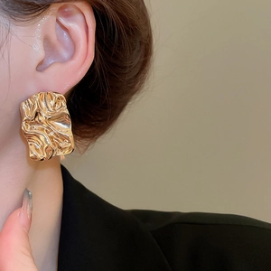 Close-up of golden irregular wrinkled rectangle stud earrings worn on ear model
