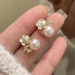 Close-up of floral pearl earrings with white enamel flower and gold branch detail