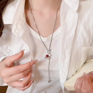 Detail of silver long necklace with a five-petal flower pendant and red center on a model