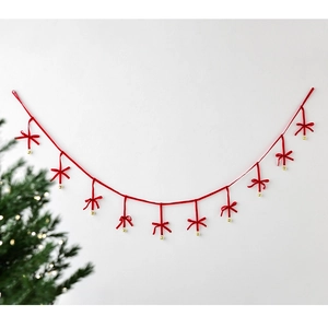 Christmas velvet bows garland with gold bells hanging on wall near a festive tree