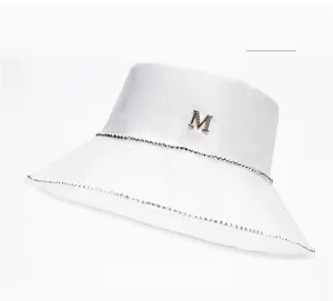 Close-up of white satin bucket hat featuring a rhinestone band and metal M logo