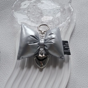 Silver bow keychain with metallic heart pendant on a minimalist textured background