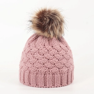 Detailed close-up of pink cable knit baby hat featuring a fluffy faux fur pompom ball